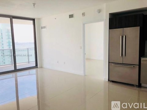 A spacious room with a large window, a white door, and a stainless steel refrigerator.