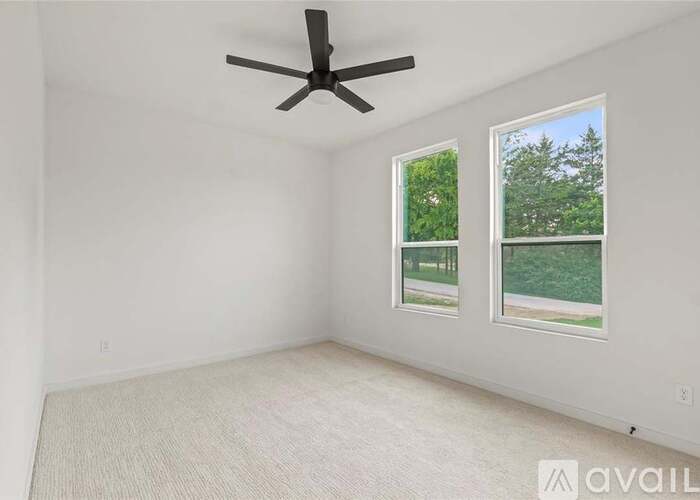 A room with a ceiling fan and two windows overlooking a green area.