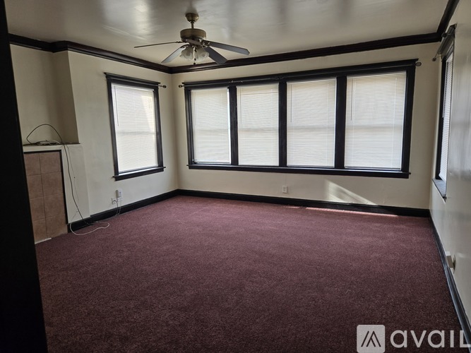 A room with a ceiling fan and large windows.