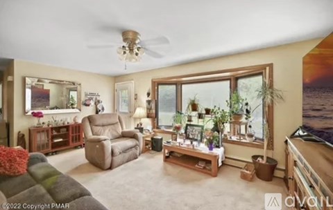 A living room with a brown couch, a chair, a table with a vase of flowers, and a large window with plants on the windowsill.