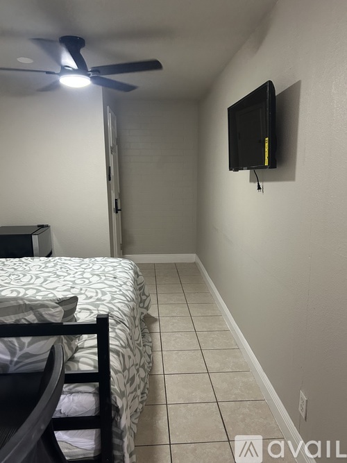 A bedroom with a bed, a ceiling fan, and a TV mounted on the wall.