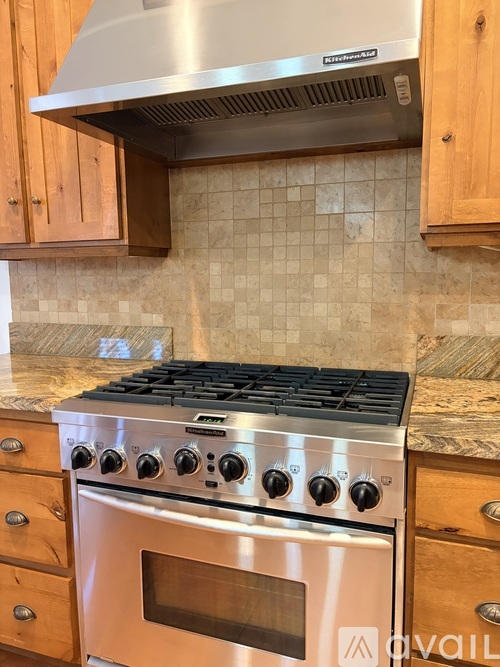 A stainless steel oven with a stove top sits in a kitchen with wooden cabinets.