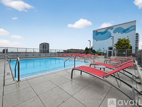 A pool with red sun loungers and a blue sky with clouds.