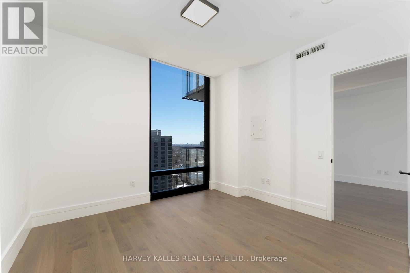 A spacious room with wooden flooring and a large window overlooking a cityscape.