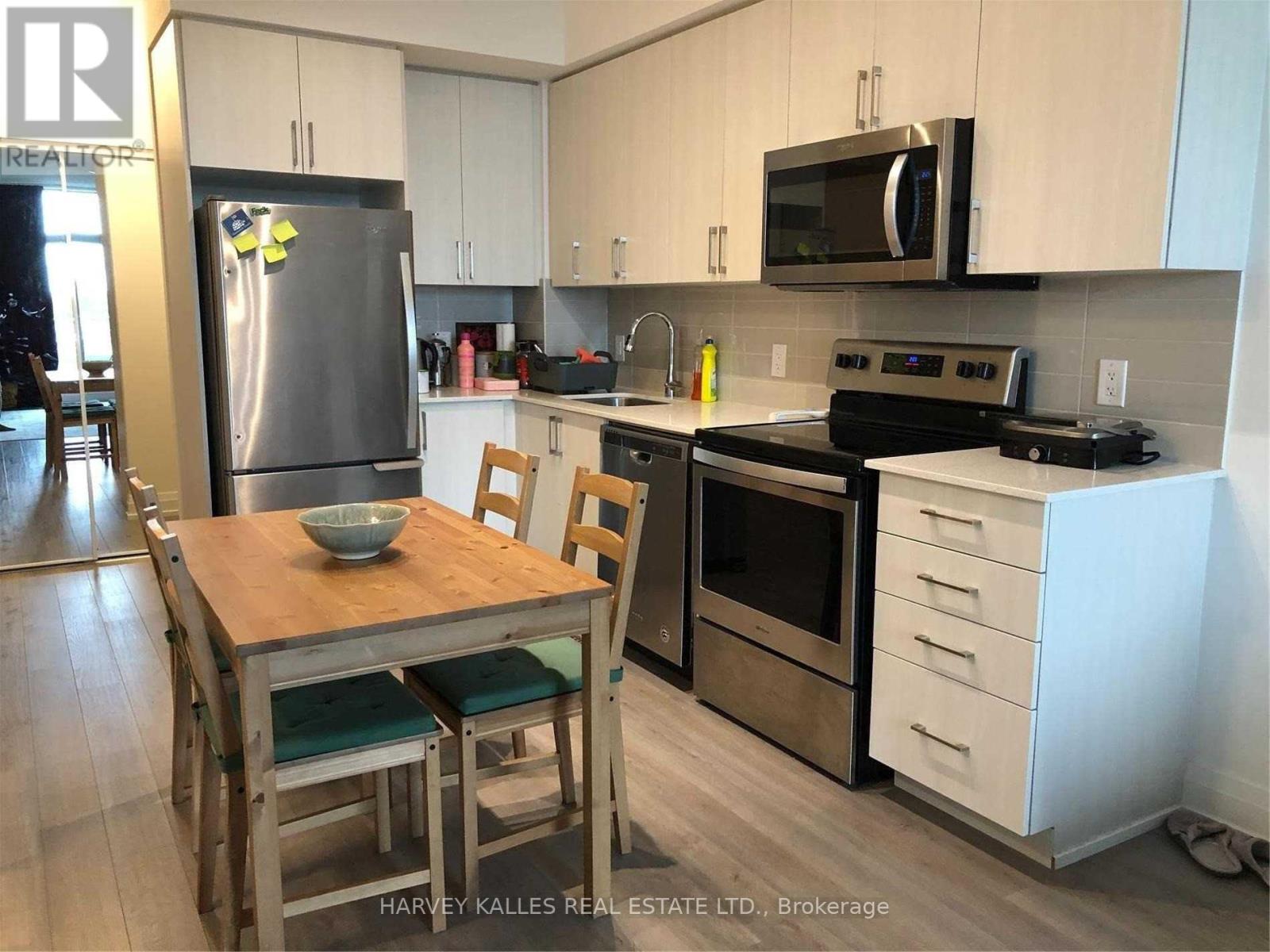 A kitchen with a wooden table and chairs, a refrigerator, a microwave, and a stove top oven.