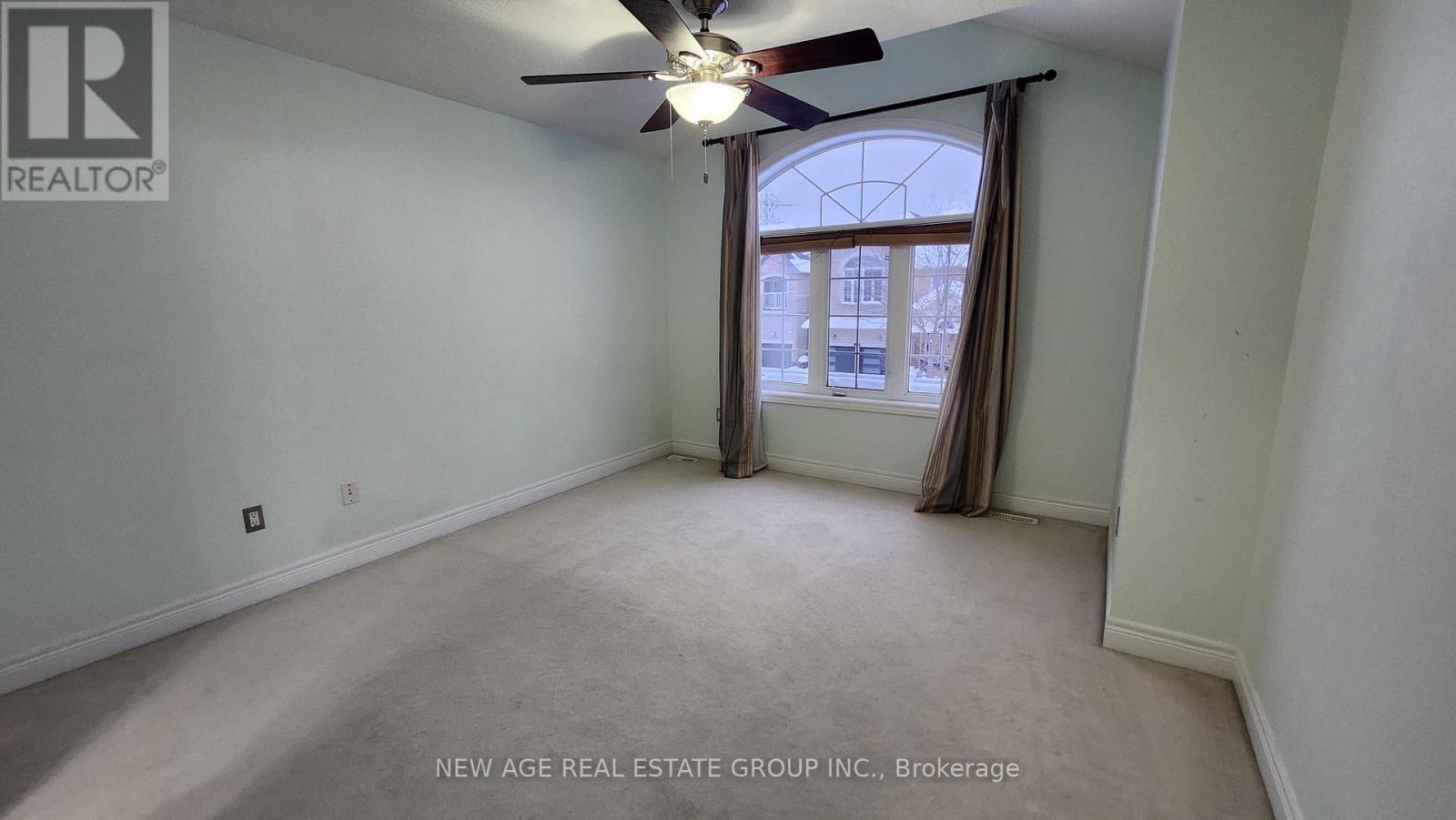 A spacious room with a ceiling fan and a window with curtains.