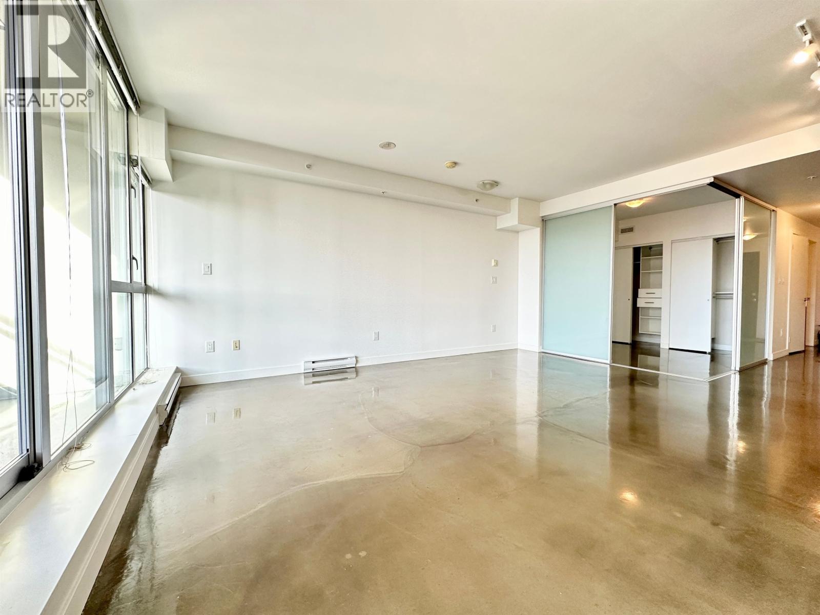 A large, empty room with a polished concrete floor and a glass wall on the left side.