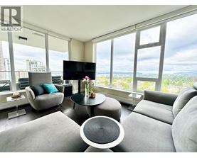 A living room with a grey sofa, a black TV and a glass table with a vase of flowers on it.