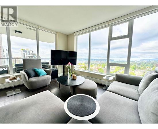 A living room with a grey sofa, a black TV and a glass table with a vase of flowers on it.