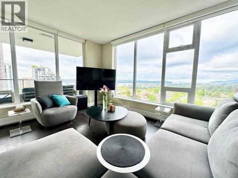 A living room with a grey sofa, a black TV and a glass table with a vase of flowers on it.