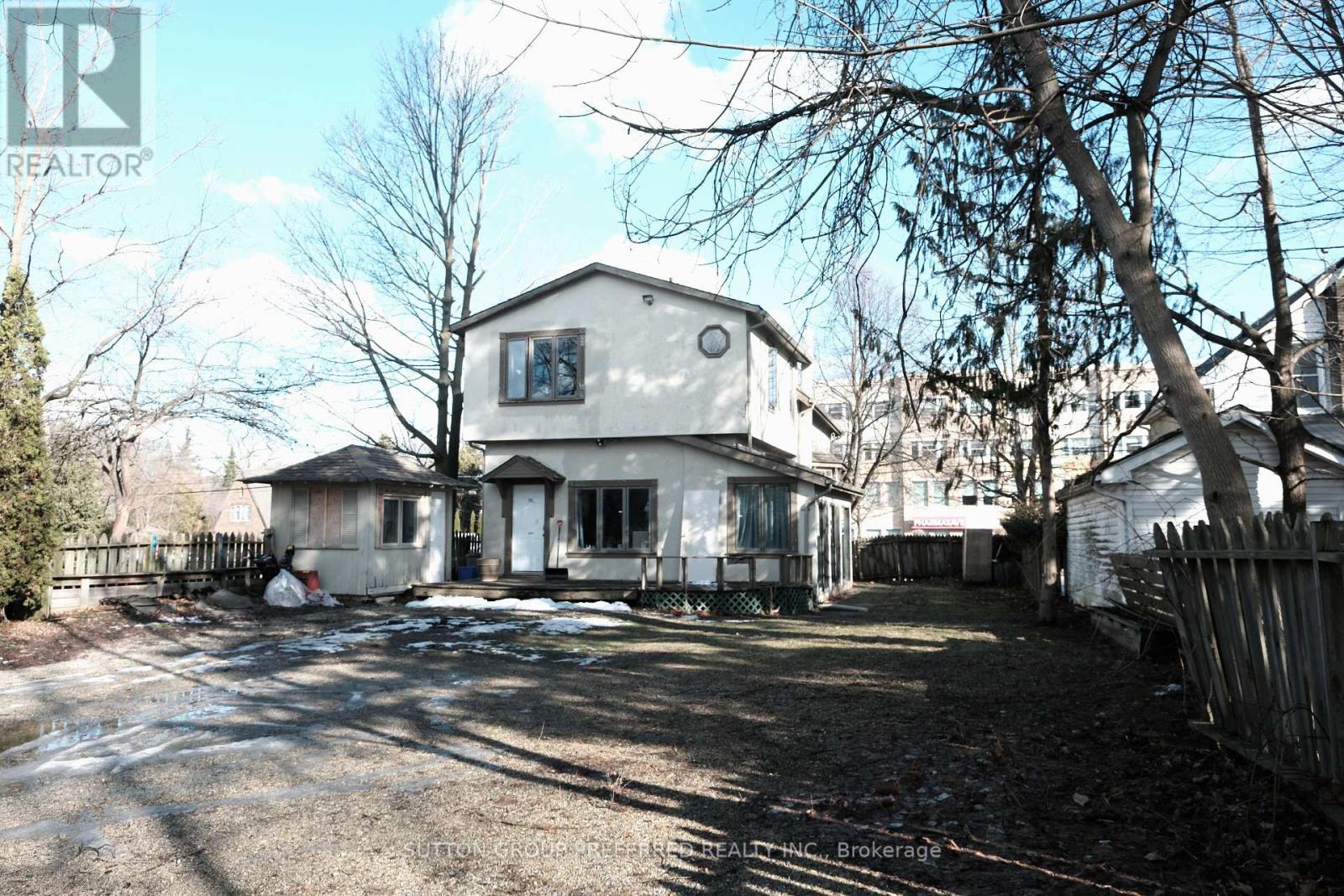 A house with a white exterior and a brown roof is surrounded by a fence and trees.