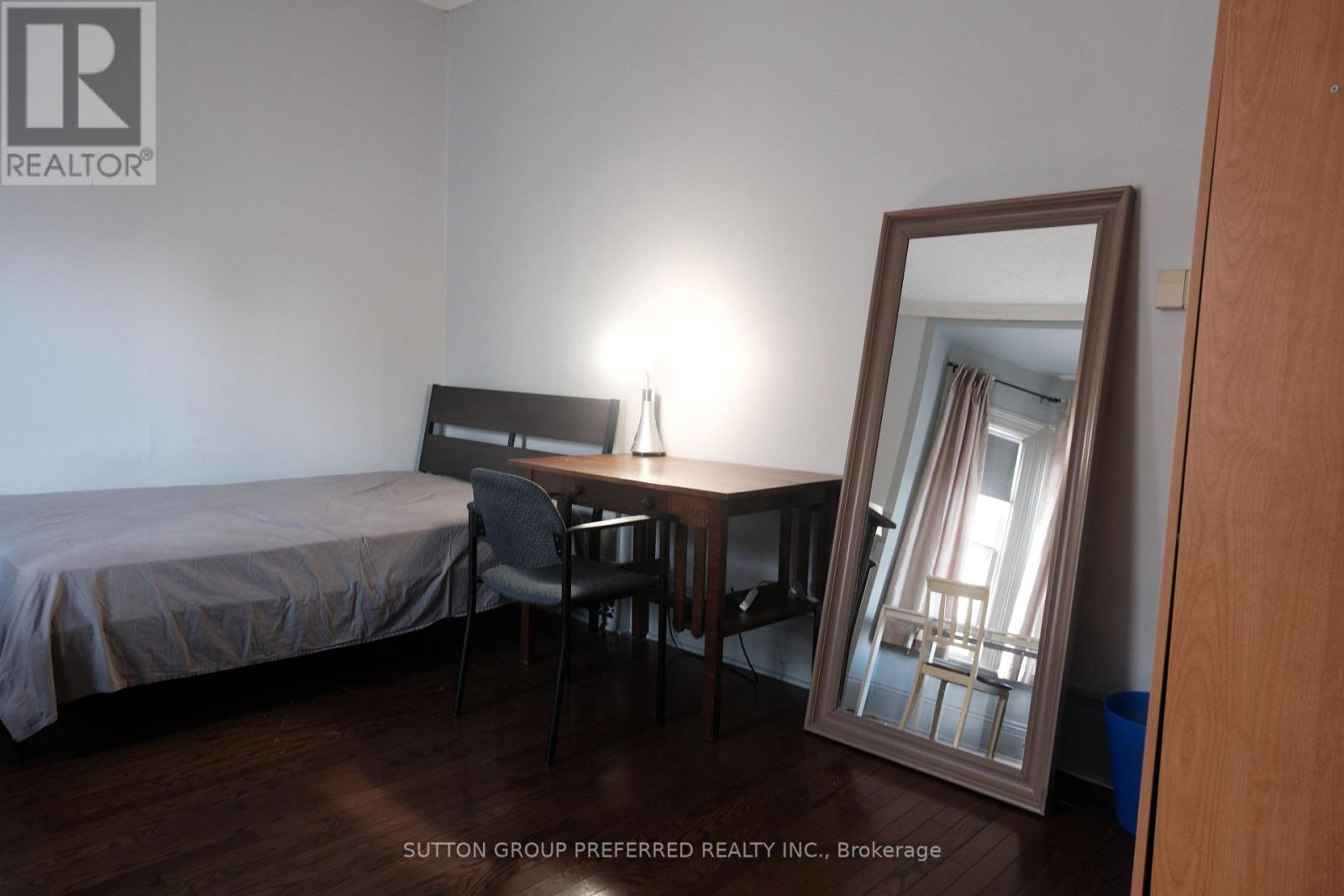 A bedroom with a bed, desk, chair and mirror.