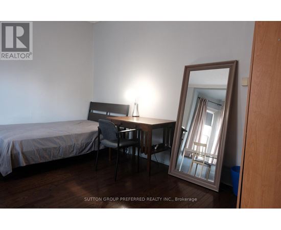 A bedroom with a bed, desk, chair and mirror.