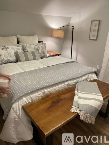 A bed with a grey and white comforter and a wooden table with a striped blanket on it.
