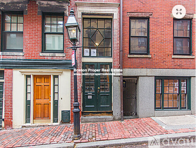 A red brick building with a green door and a sign that says "Boston Proper Real Estate.".