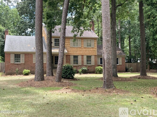 A house with a brown roof and white trim is surrounded by trees.
