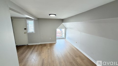 A room with wooden flooring and white walls, with a door and a window.