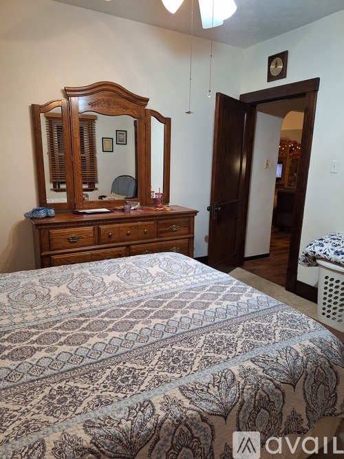 A bedroom with a bed, dresser, mirror and a clock on the wall.