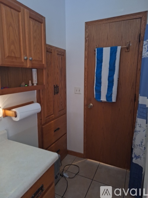 A bathroom with a toilet, wooden cabinets, and a striped towel hanging on the door.