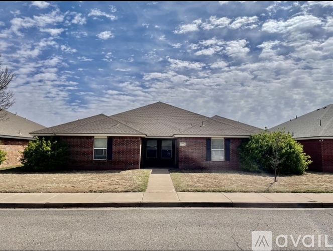 A brick house with a tree in front and a cloudy sky above.