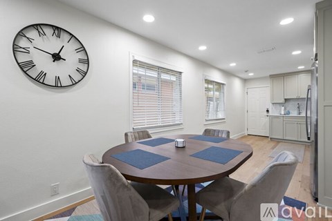 A dining room with a table and chairs and a clock on the wall.