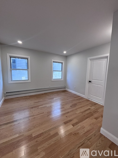 A room with wooden flooring and two windows.