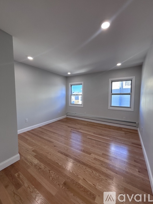 A room with wooden flooring and two windows.