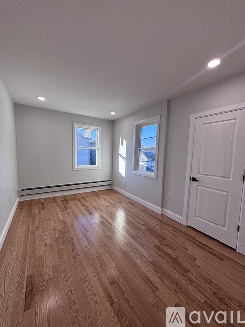 A room with wooden flooring and two windows.