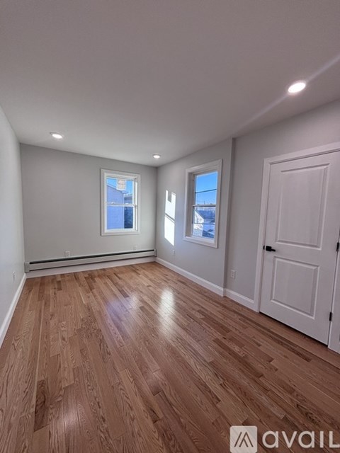 A room with wooden flooring and two windows.