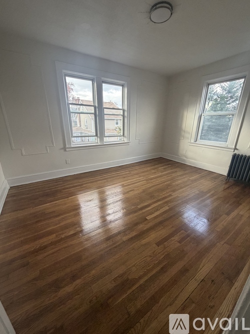 A room with wooden flooring and two windows.