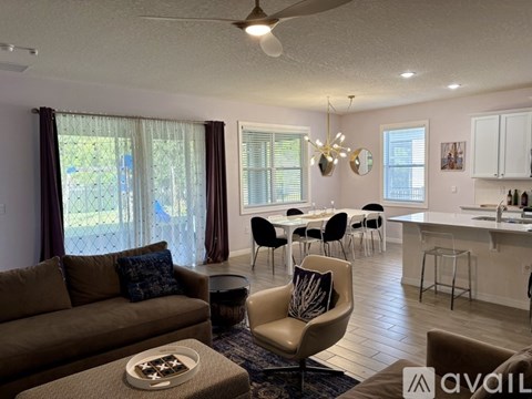 A living room with a brown couch and a dining area with white chairs.