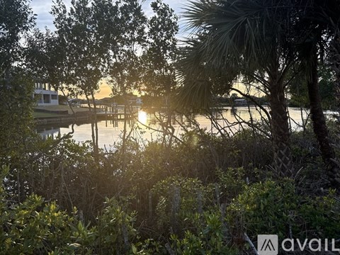 A sunset view of a lake with trees and a house in the background.