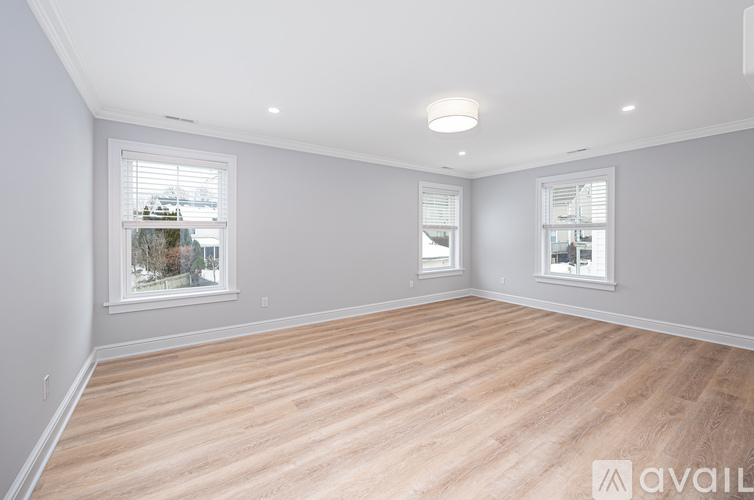 A spacious room with wooden flooring and two windows.