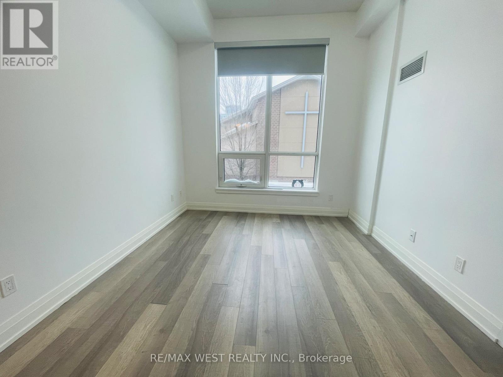 A room with wooden flooring and a window showing a building outside.