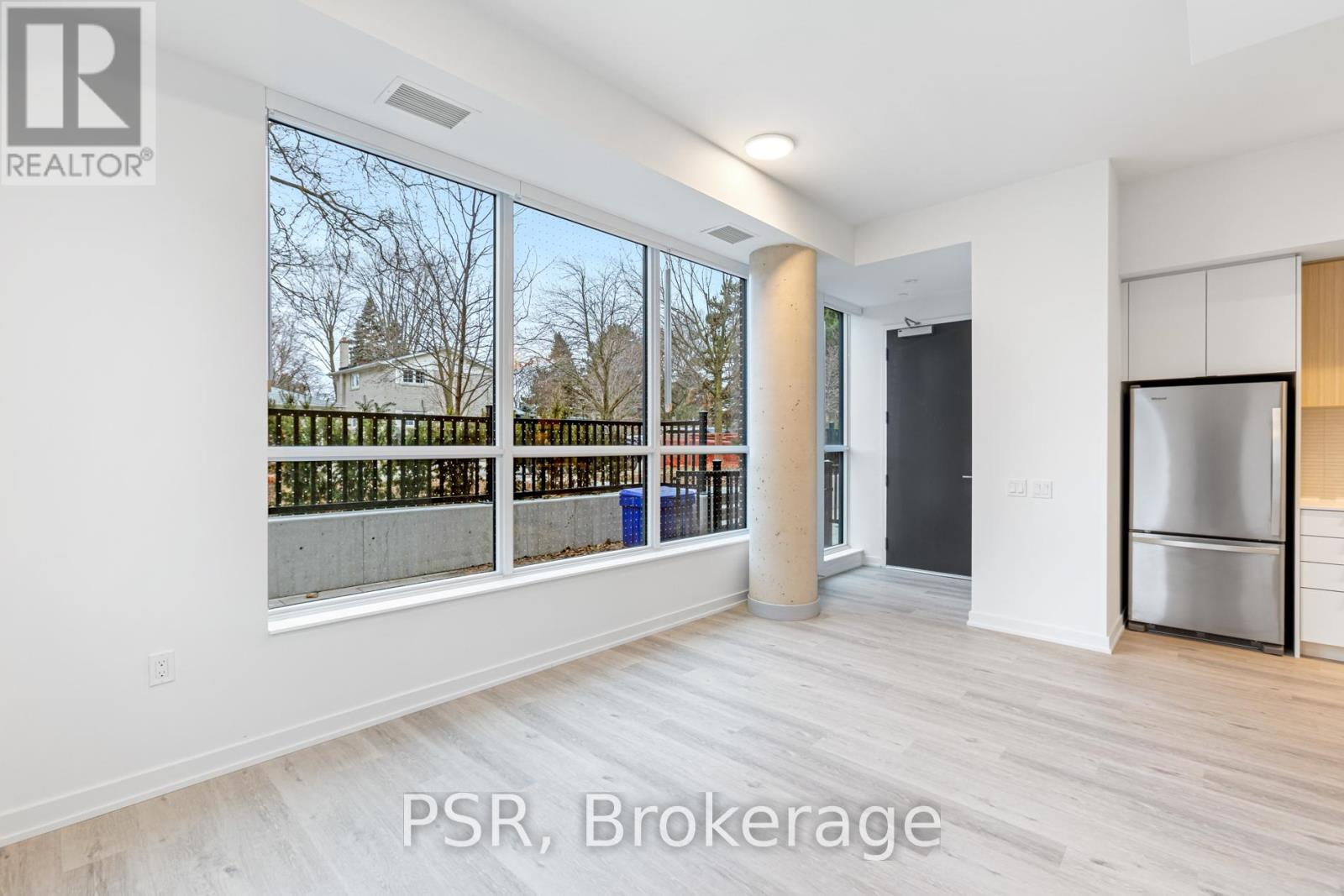 A spacious room with a view of a fence and trees through the windows.