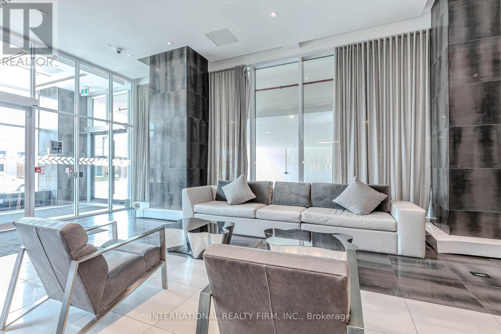 A modern living room with a glass wall and a grey sofa.
