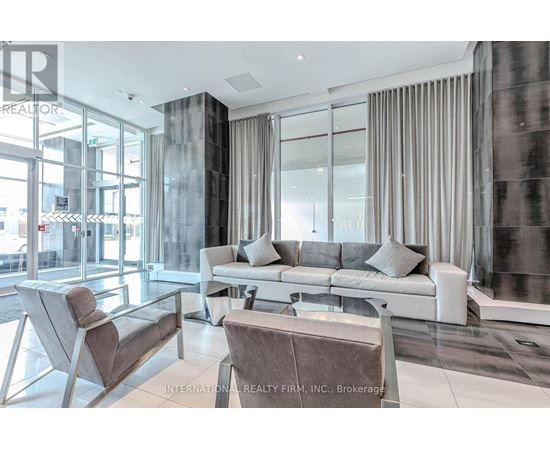 A modern living room with a glass wall and a grey sofa.
