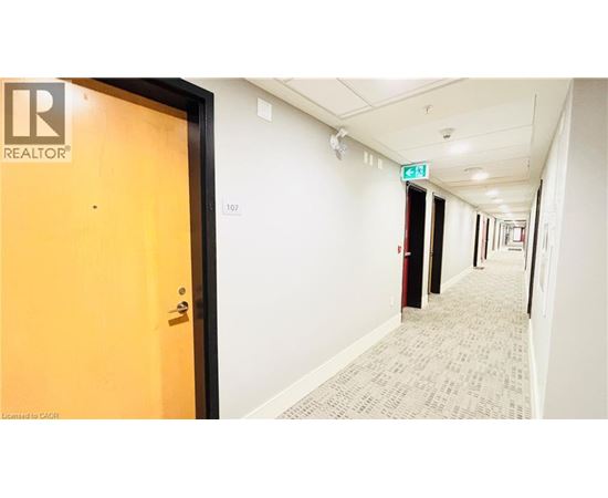 A hallway with a door on the left and a green exit sign above the door.