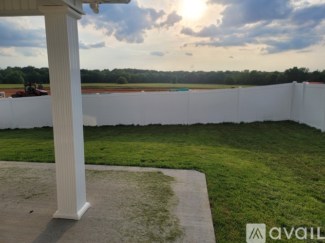 A white pillar stands in a yard with a white fence and a field in the background.