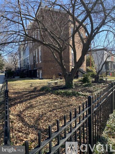 A tree in front of a brick building with a black fence in the foreground.