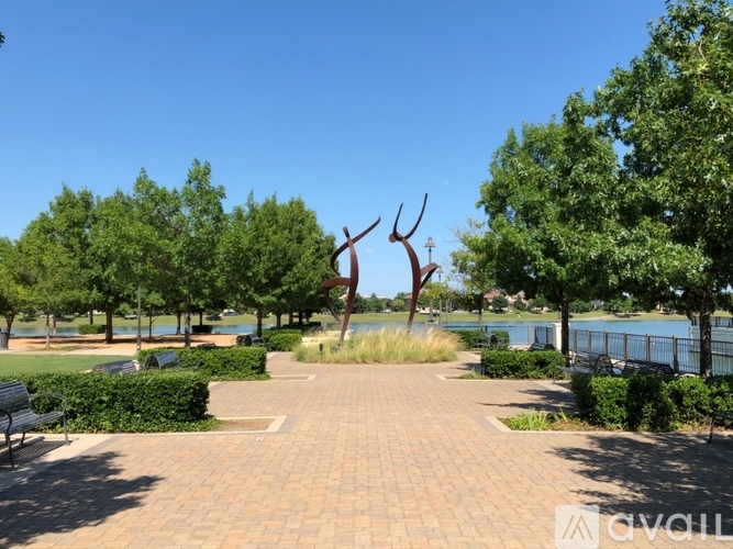 A park with a bench, trees, and a sculpture in the middle of a brick path.