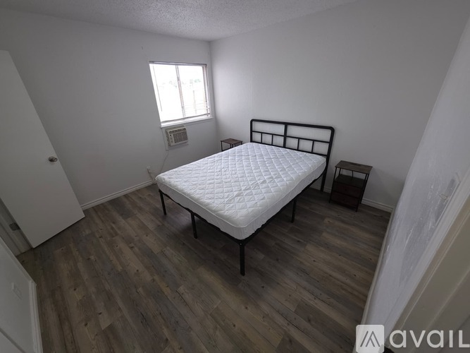 A room with wooden flooring and white walls, leading to another room.