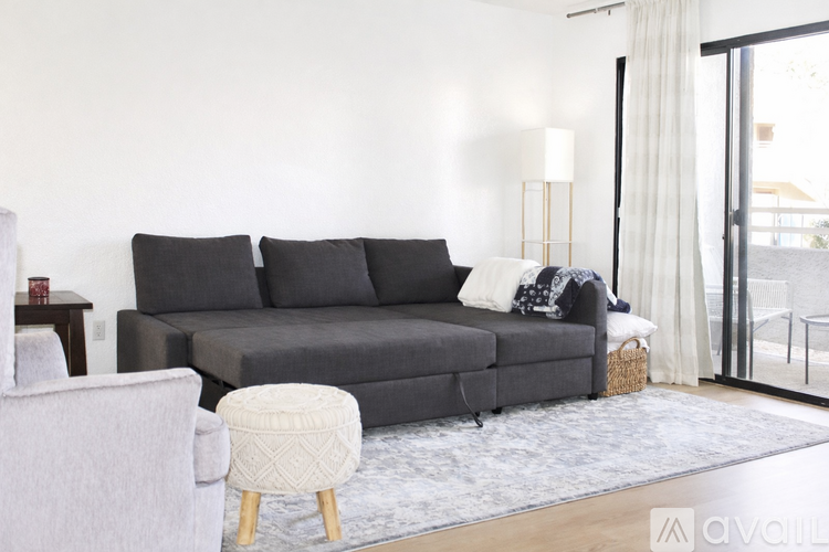 A living room with a black sofa, a table with a cup and a bottle, a chair, and a ceiling fan.