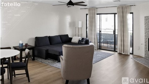 A living room with a black sofa, a table with a cup and a bottle, a chair, and a ceiling fan.