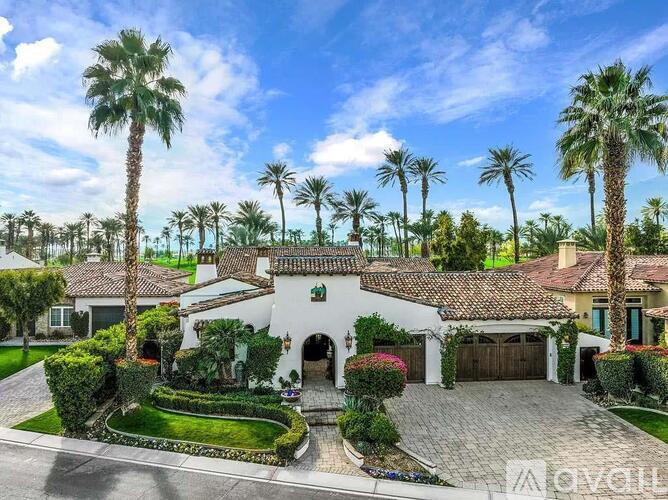 A large house with a driveway and palm trees in front.