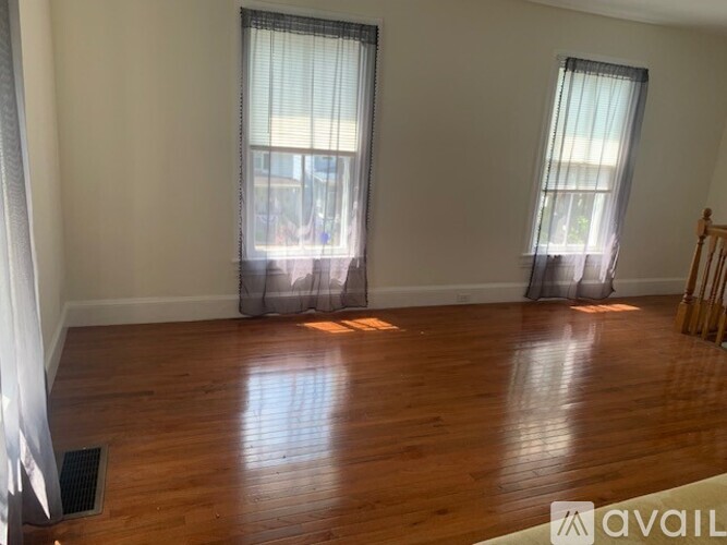 A room with wooden floors and two windows with curtains.