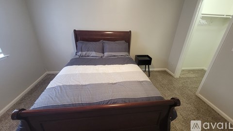 A bed with a wooden headboard and a striped comforter is in a room with a carpeted floor.