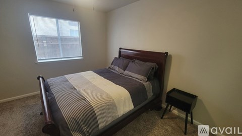A bedroom with a bed, a small table, and a window with blinds.