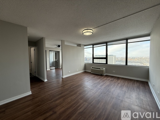A spacious room with wooden floors and large windows overlooking a cityscape.