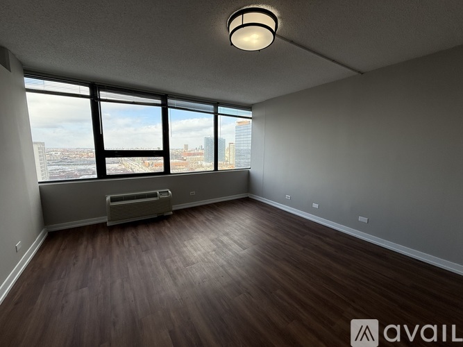 A spacious room with wooden floors and large windows overlooking a cityscape.